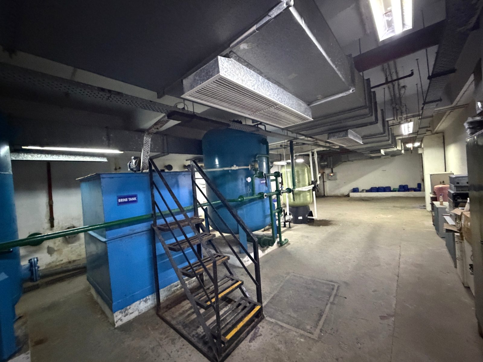 Rectangular blue tank with access stair and pipework in the basement plant area