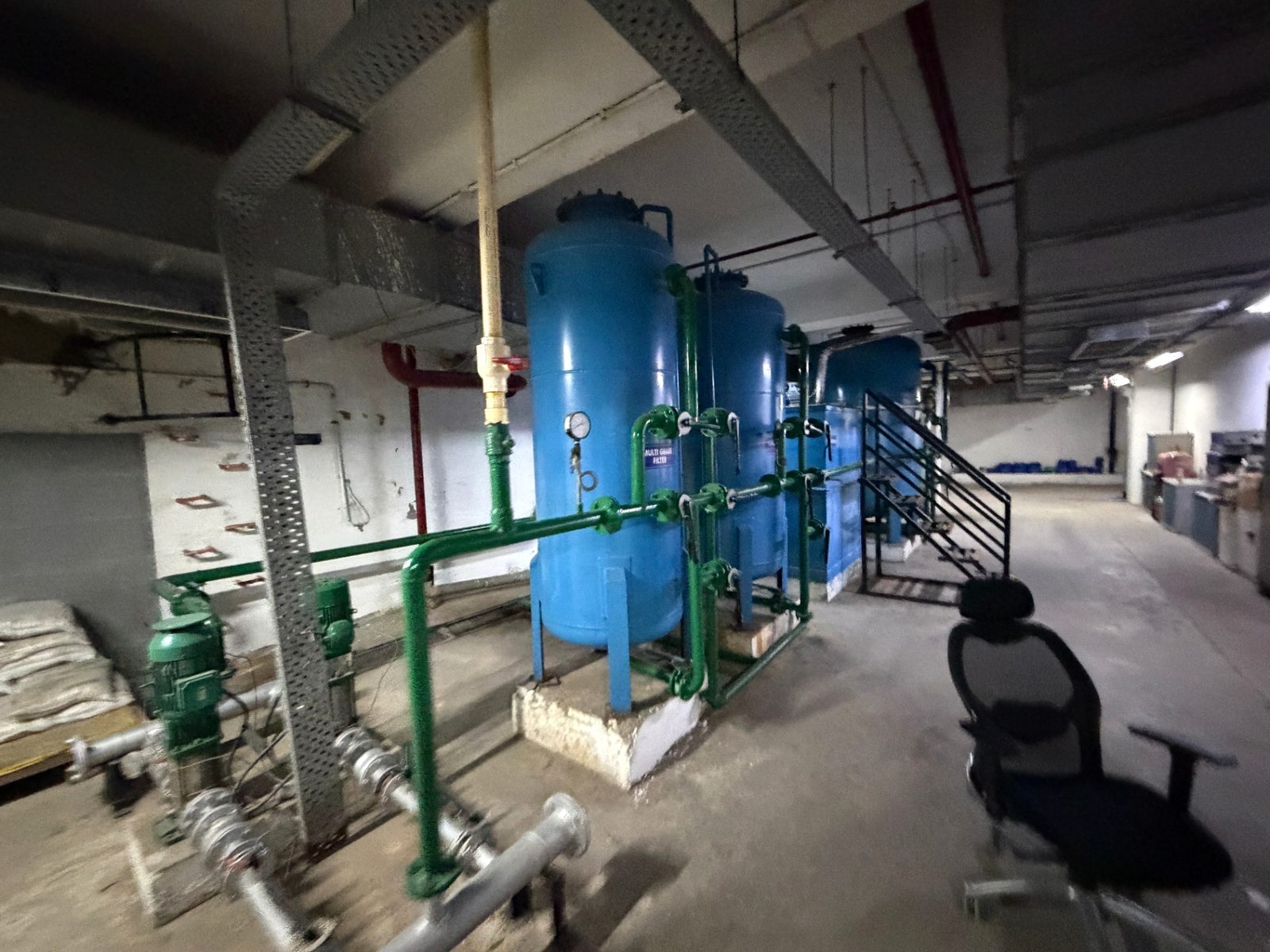 Blue filter vessels with gauges, green pipework and pumps in a basement plant area