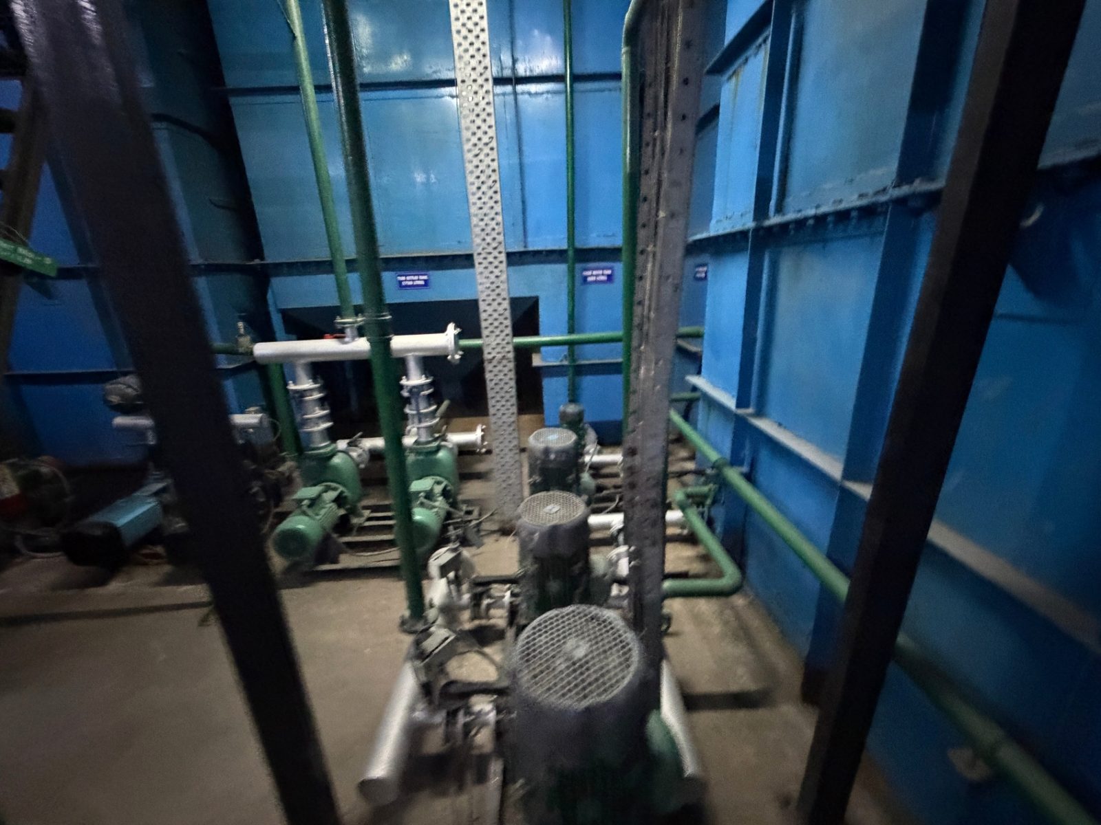 Close view of pump motors and pipework between fabricated blue tanks