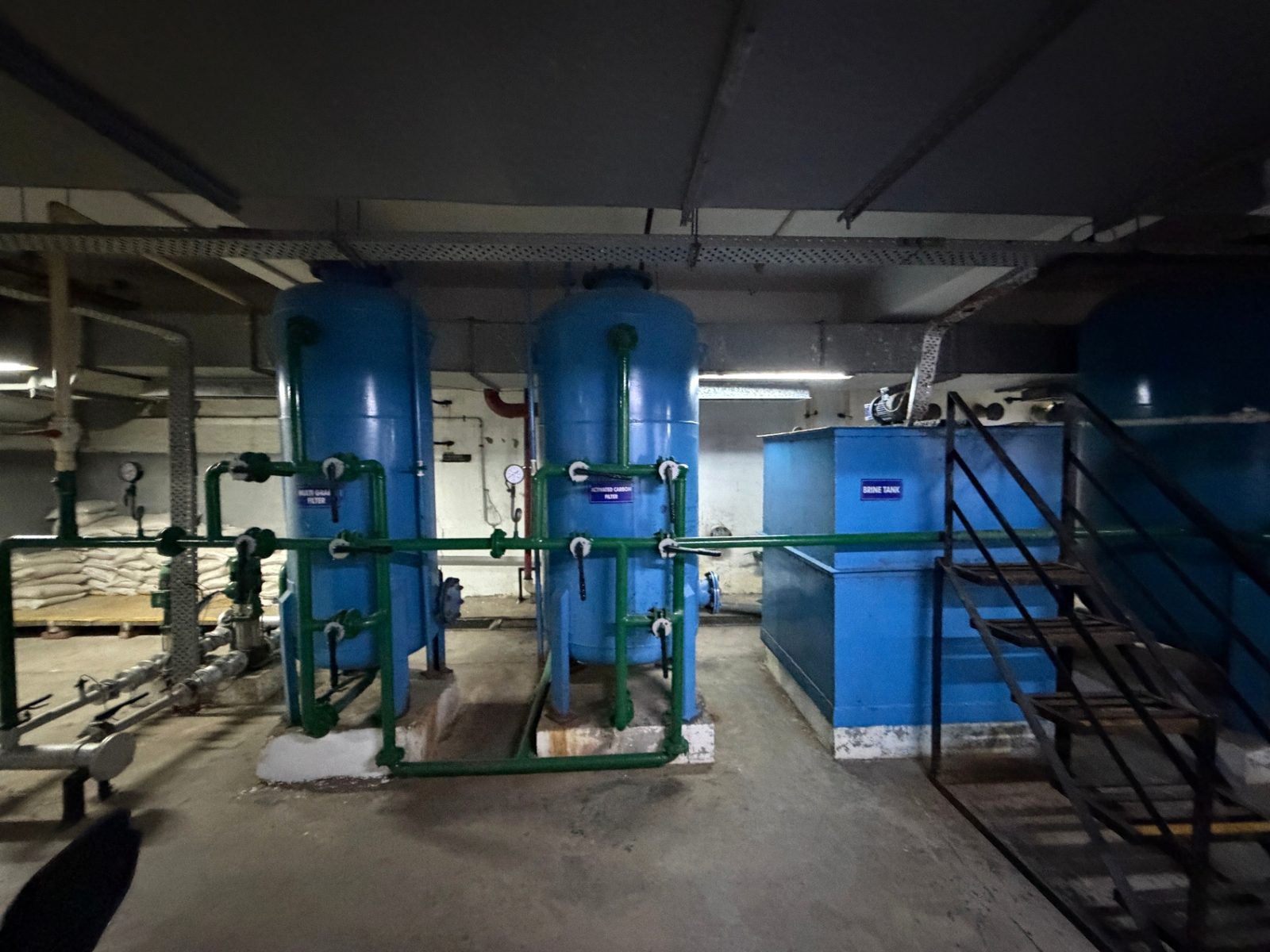 Two blue pressure filter vessels with green pipework beside a rectangular tank and access stair