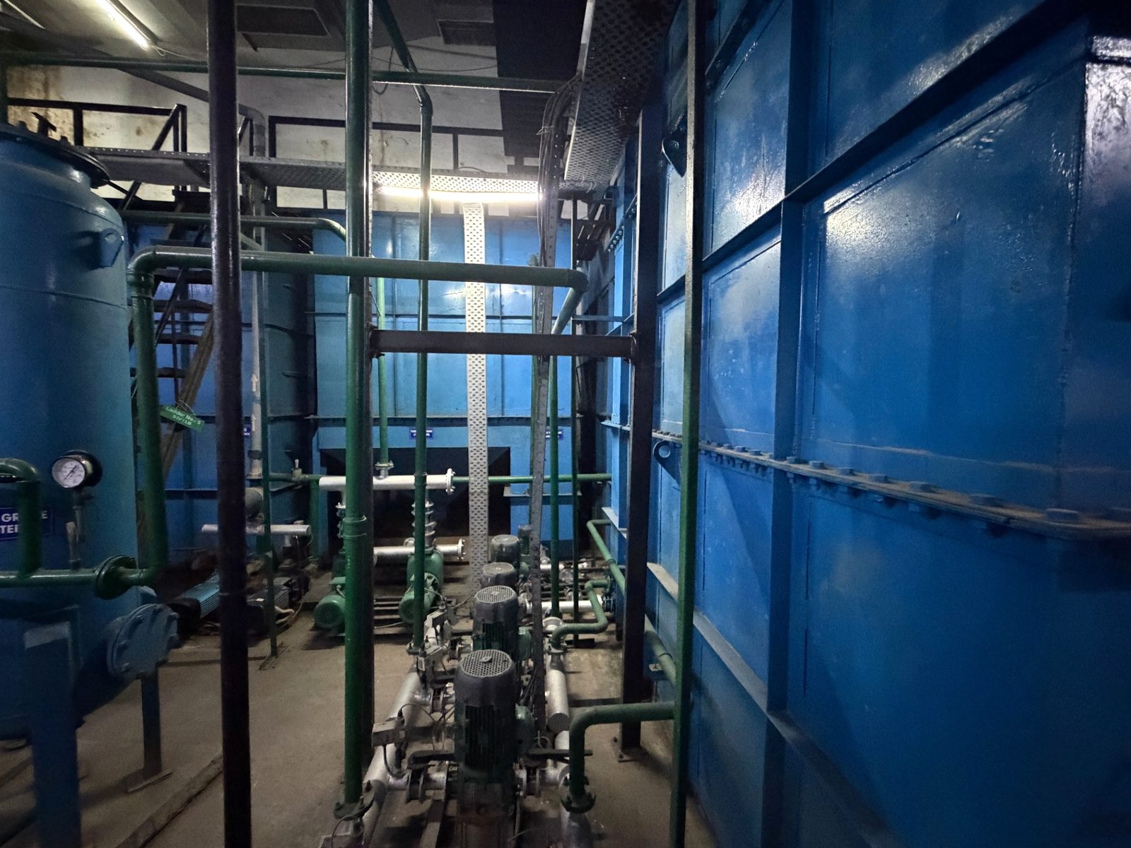 Pressure vessel with gauge, pump set and pipe supports beside a fabricated tank wall